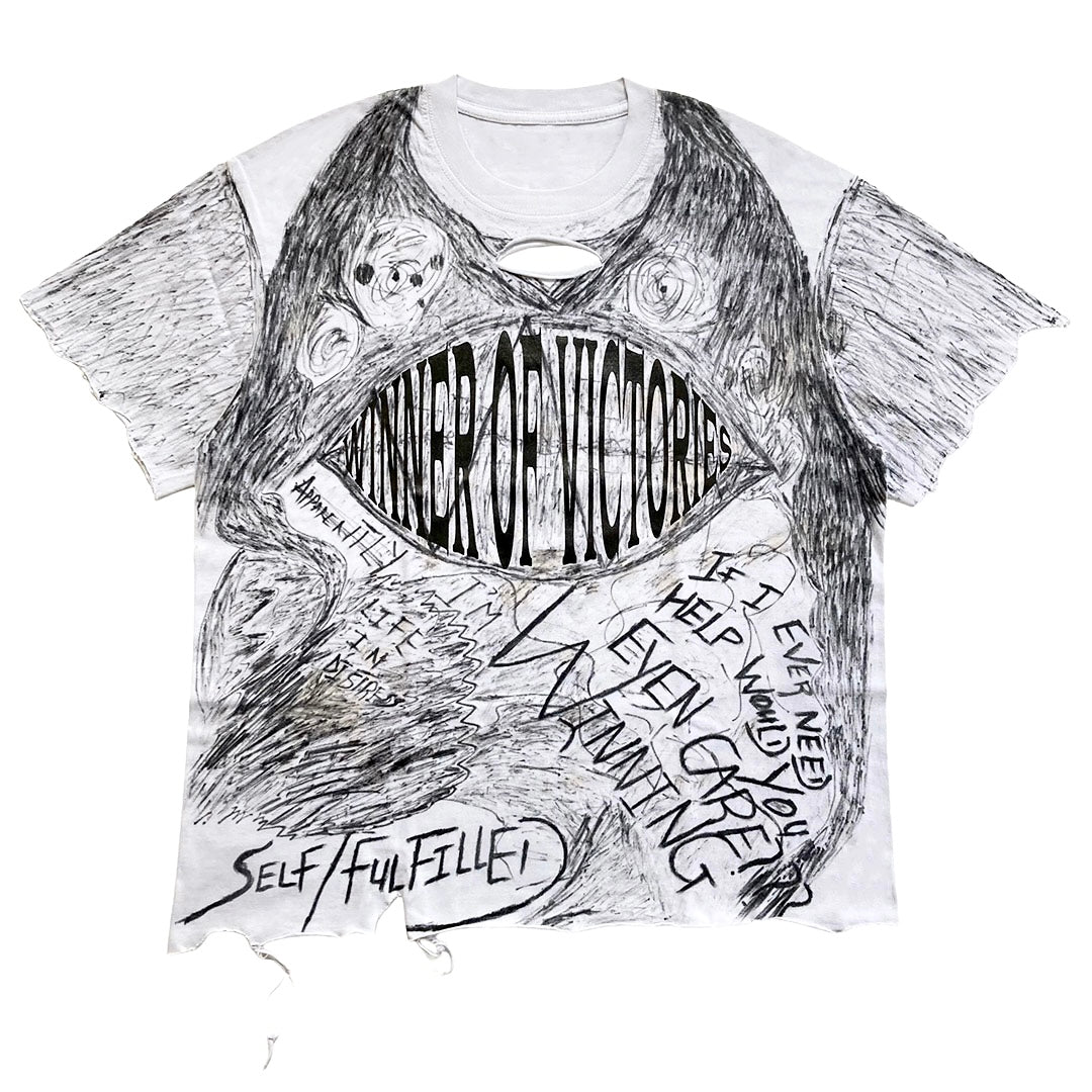 A white short-sleeve t-shirt with a distressed, hand-drawn black ink sketch of a monster or creature. The graphic features the text 'WINNER OF VICTORIES' inside a large eye, 'SELF/FULFILLME!' in a circle, and other motivational phrases written in a sketchy style.