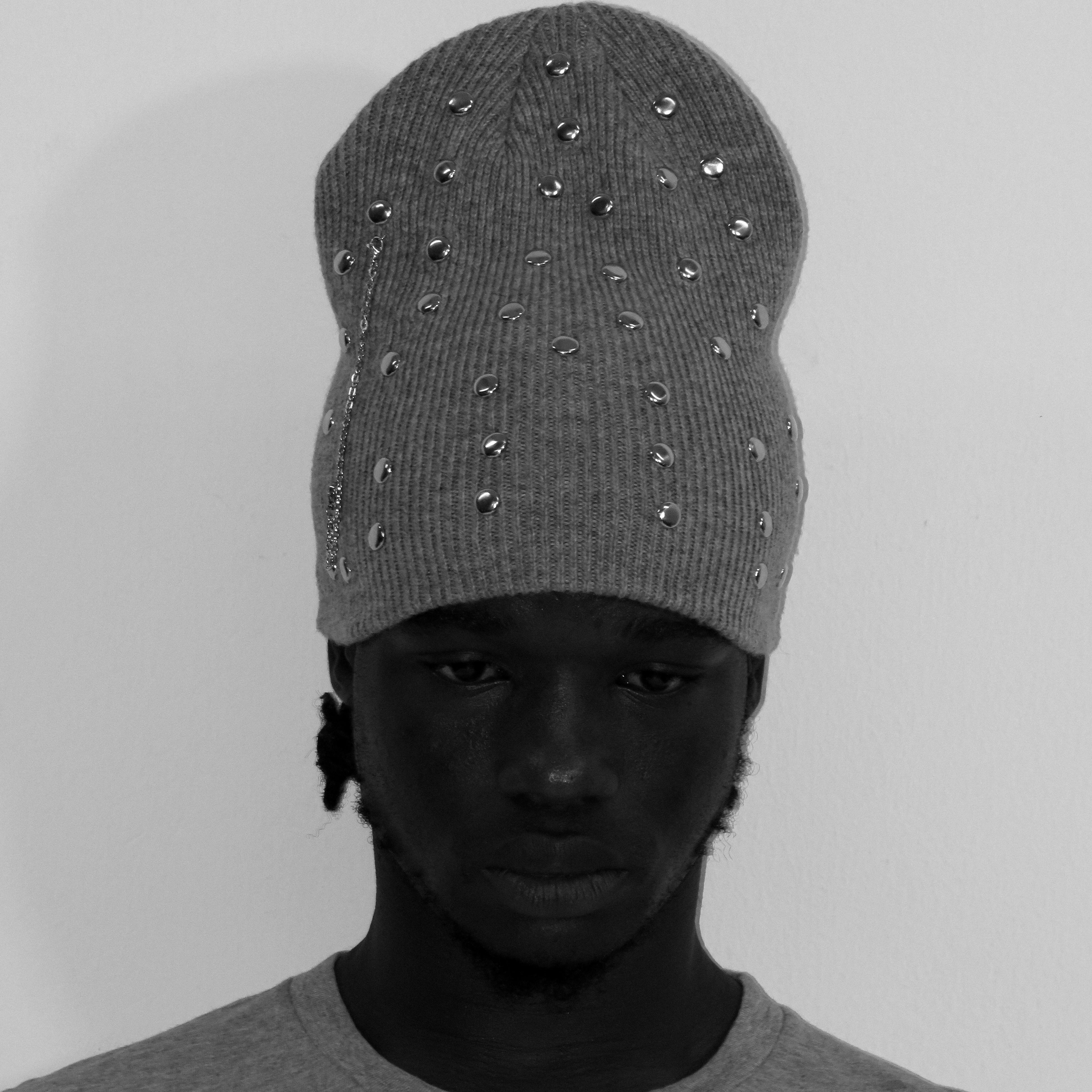 Person wearing a gray beanie with decorative studs on a plain background