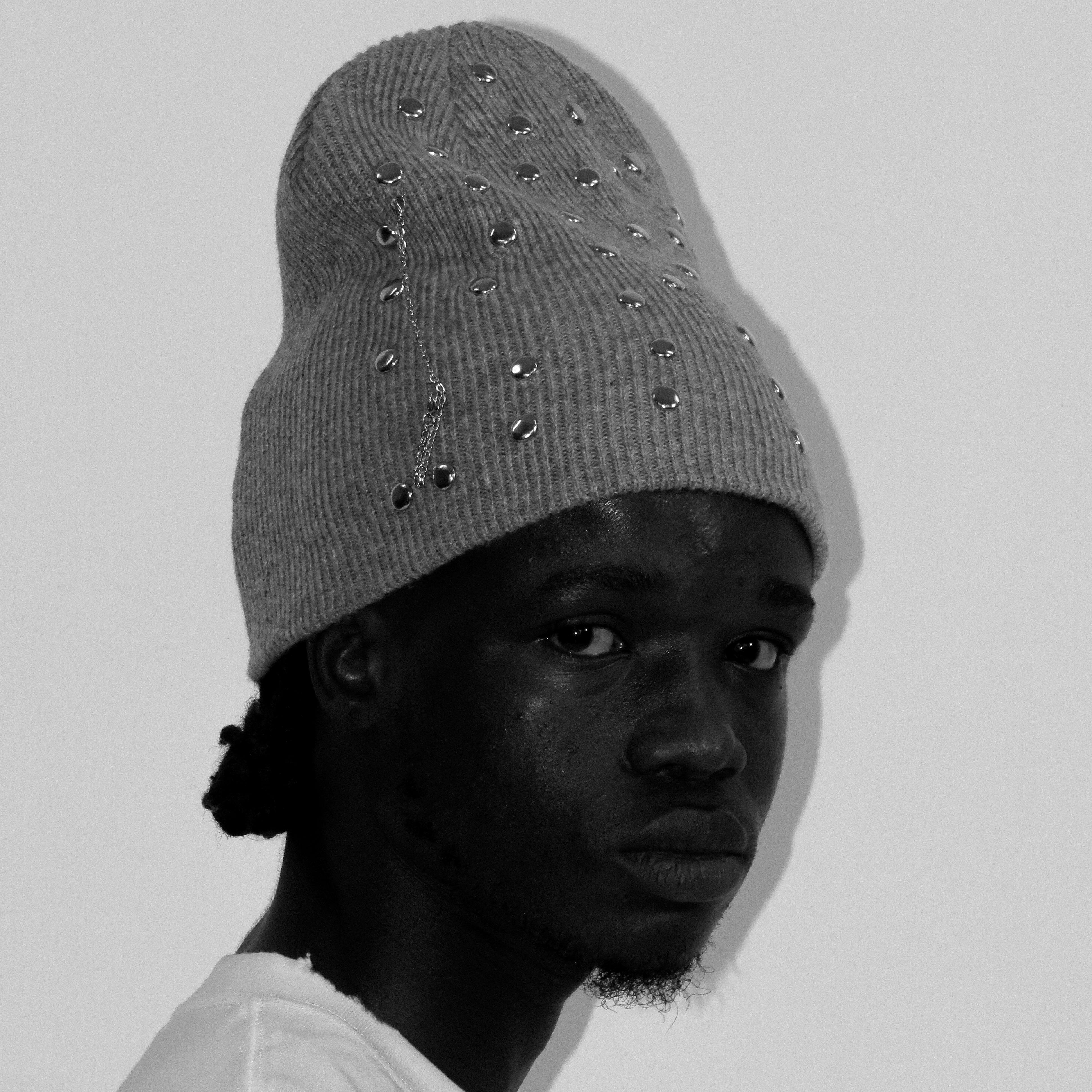Person wearing a gray beanie with decorative elements on a plain background
